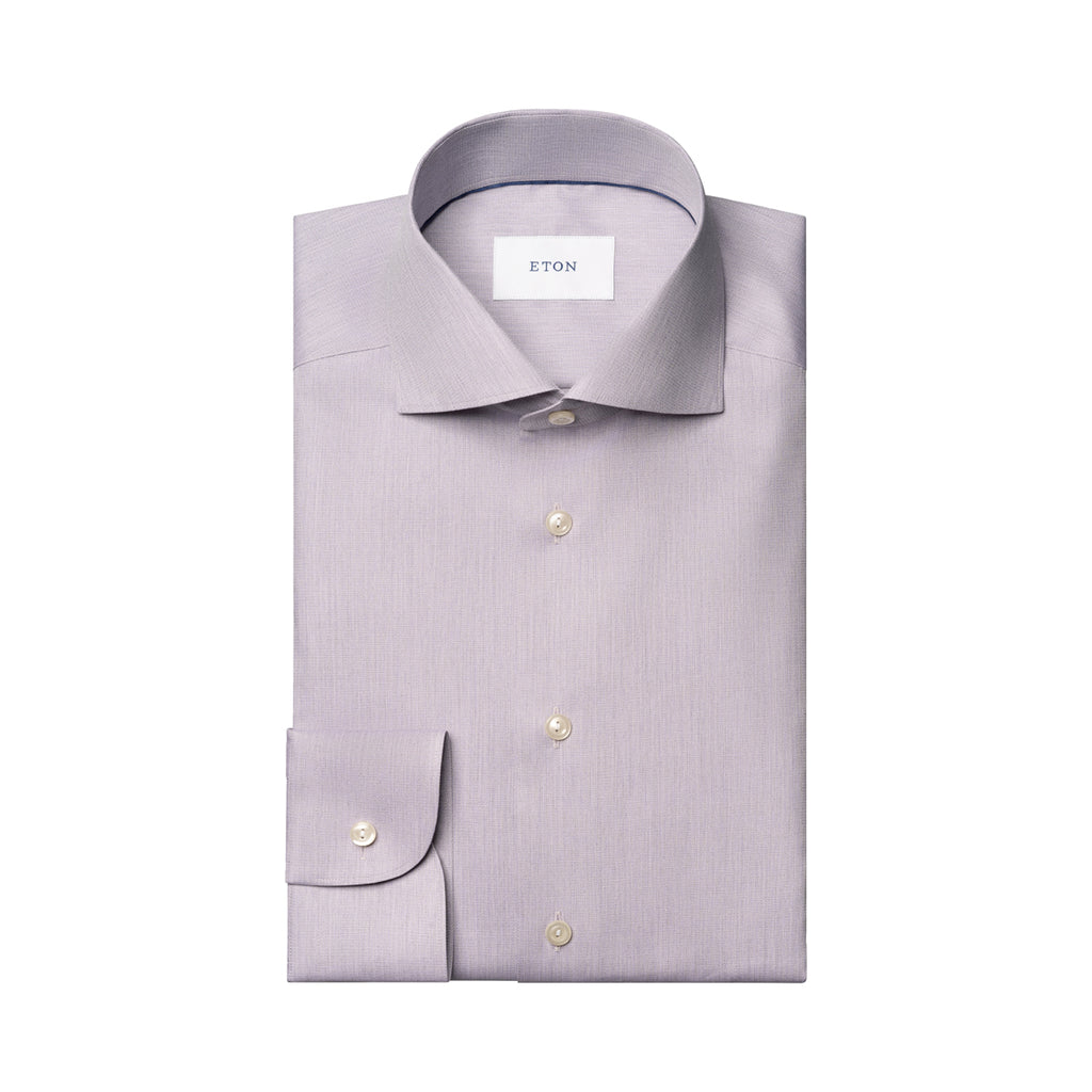 A light lavender dress shirt by ETON, neatly folded to show the collar, front buttons, and single-button cuff, on a solid white background. Eton Shirt available at Sakks Menswear in Southampton.