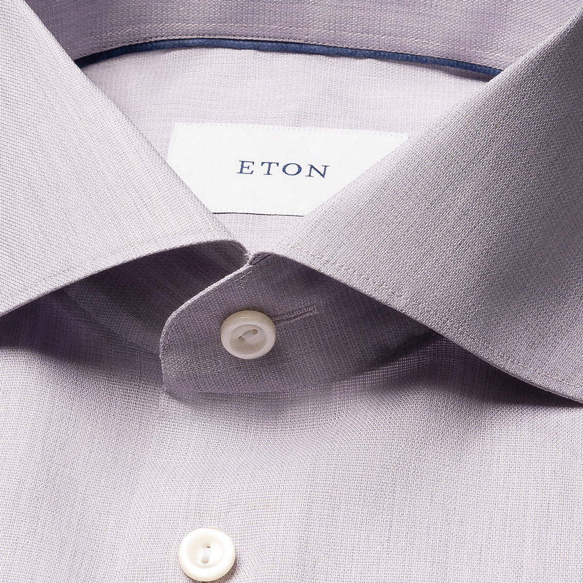 Close-up of a light lavender dress shirt collar with a white button and a visible ETON neck label. Eton Shirt available at Sakks Menswear in Southampton.