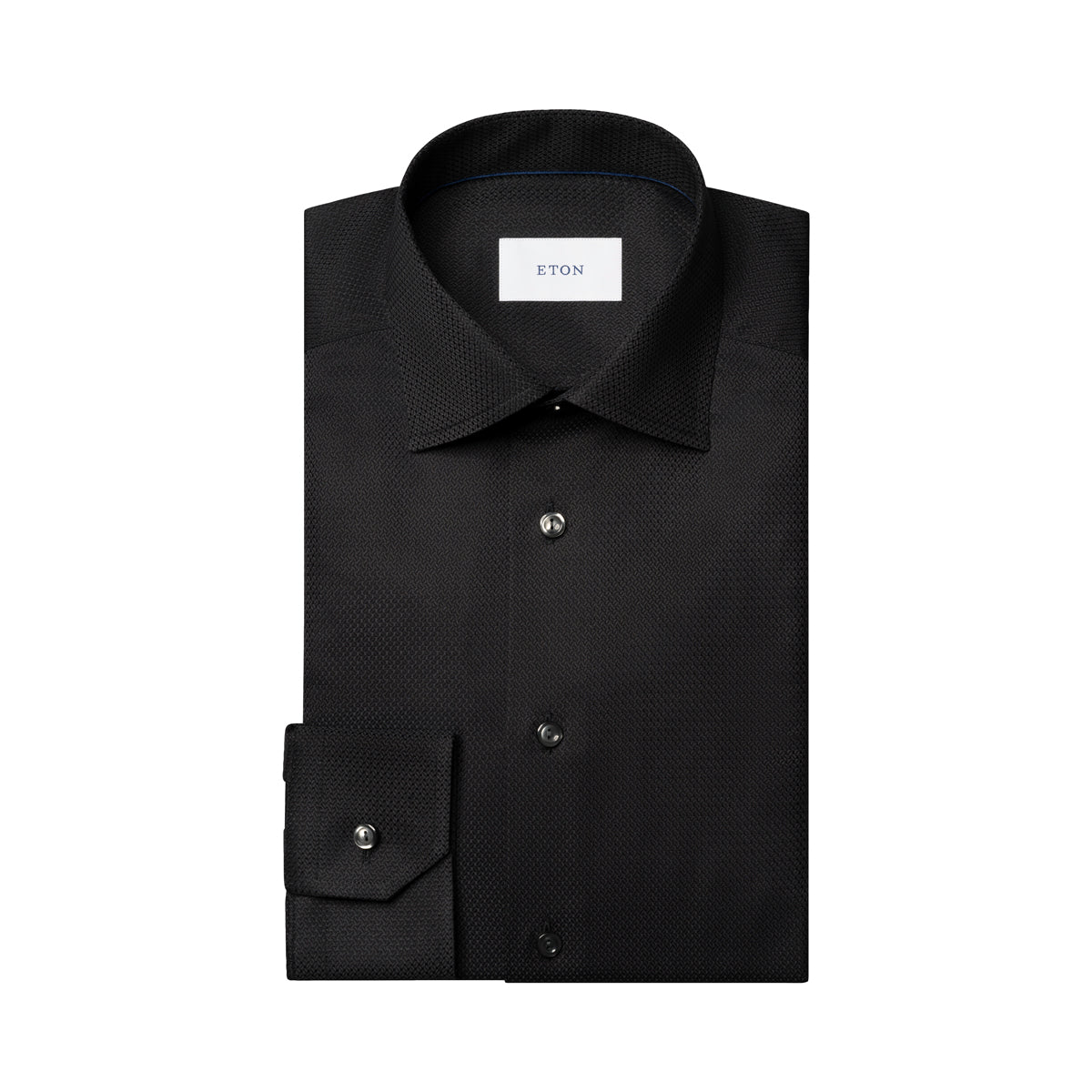 A folded black long-sleeve dress shirt with a subtle micro-texture pattern, featuring a pointed collar, button-down front, and a single-button cuff. The brand label 'ETON' is visible inside the collar. Eton Shirt available at Sakks Menswear in Southampton.