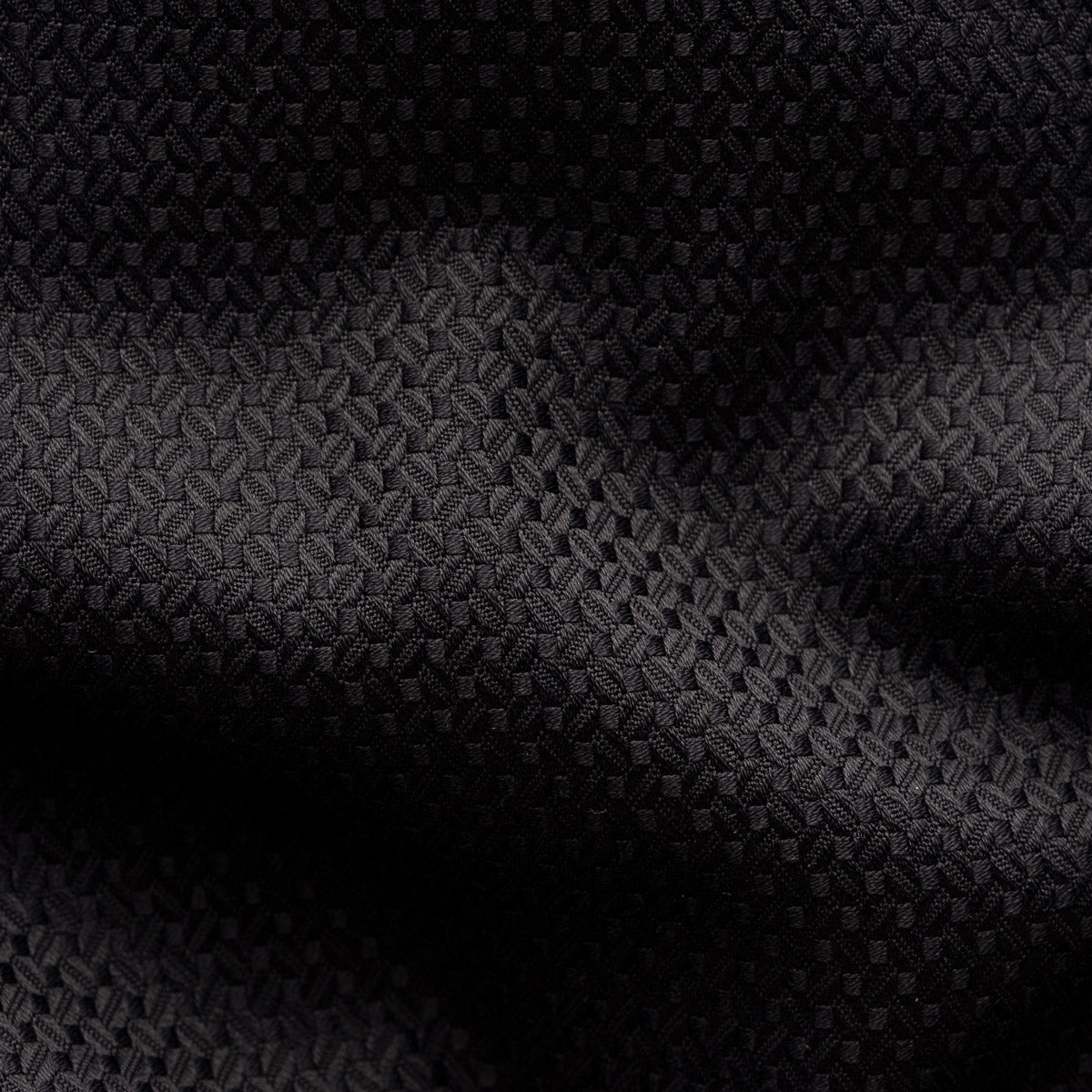 A close-up of a black textured fabric with a subtle woven geometric pattern and soft shadows across the surface. Eton Shirt available at Sakks Menswear in Southampton.