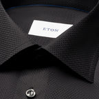 Close-up of a dark charcoal textured dress shirt collar with a white neck label reading ETON. Eton Shirt available at Sakks Menswear in Southampton.