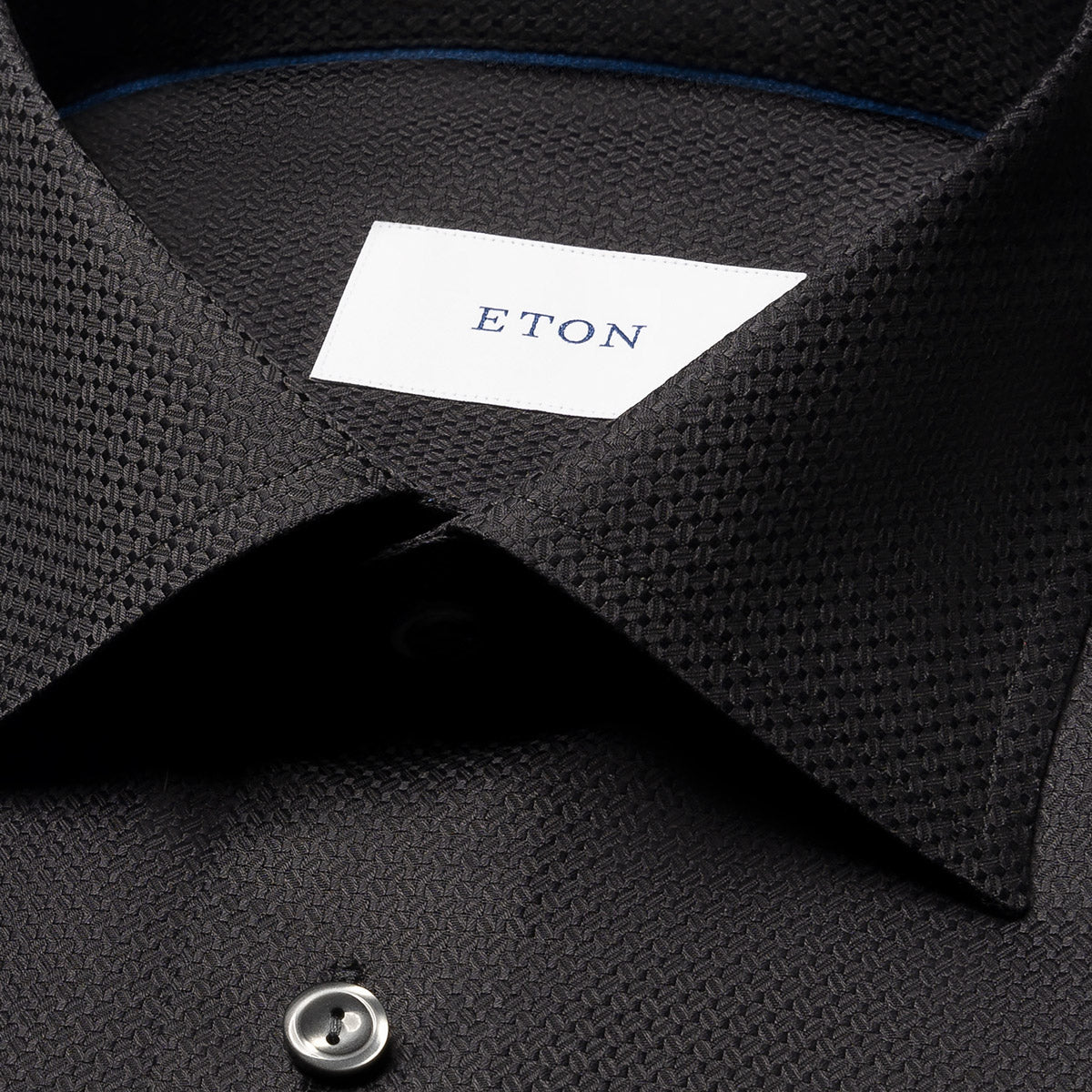 Close-up of a dark charcoal textured dress shirt collar with a white neck label reading ETON. Eton Shirt available at Sakks Menswear in Southampton.