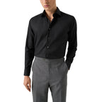 A man wearing a black long-sleeve button-down dress shirt tucked into gray trousers, shown from the chin down against a plain white background. Eton Shirt available at Sakks Menswear in Southampton.