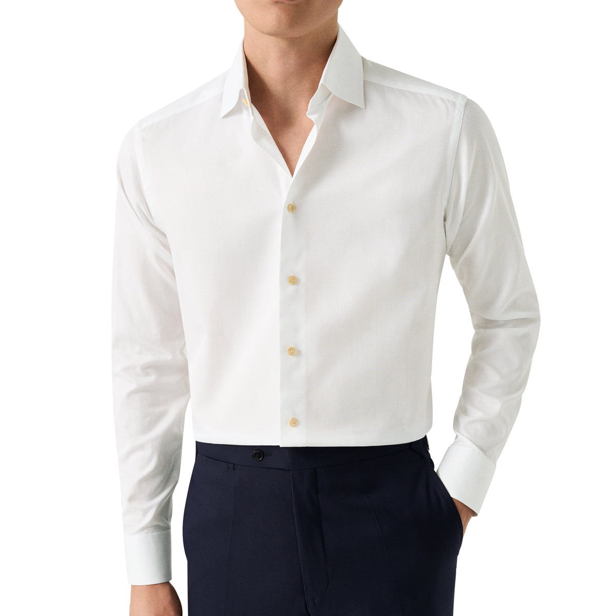 A man wearing a crisp white long-sleeve button-down dress shirt with light-coloured buttons, paired with dark navy trousers, shown from the chin down on a plain white background. Eton Shirt available at Sakks Menswear in Southampton.