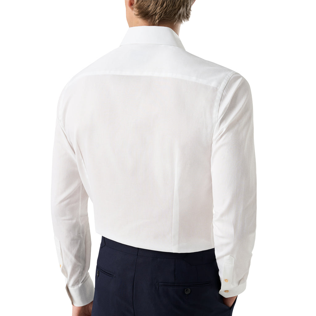 A man viewed from the back wearing a crisp white long-sleeve dress shirt and dark navy trousers, against a plain white studio background. Eton Shirt available at Sakks Menswear in Southampton.