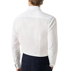 A man viewed from the back wearing a crisp white long-sleeve dress shirt and dark navy trousers, against a plain white studio background. Eton Shirt available at Sakks Menswear in Southampton.