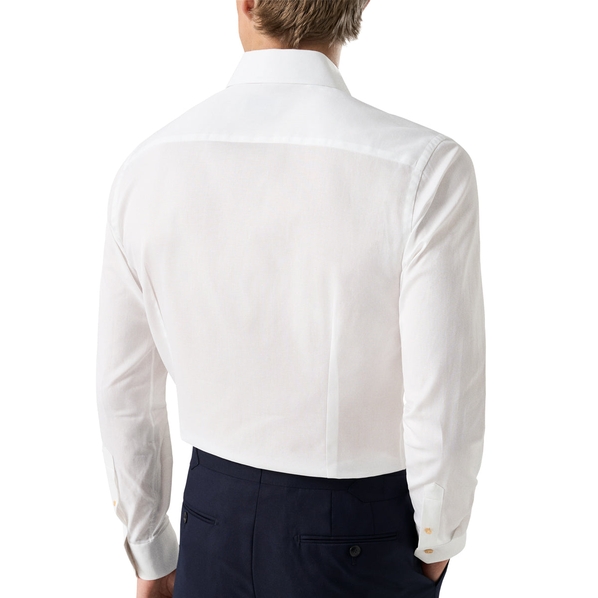 A man viewed from the back wearing a crisp white long-sleeve dress shirt and dark navy trousers, against a plain white studio background. Eton Shirt available at Sakks Menswear in Southampton.