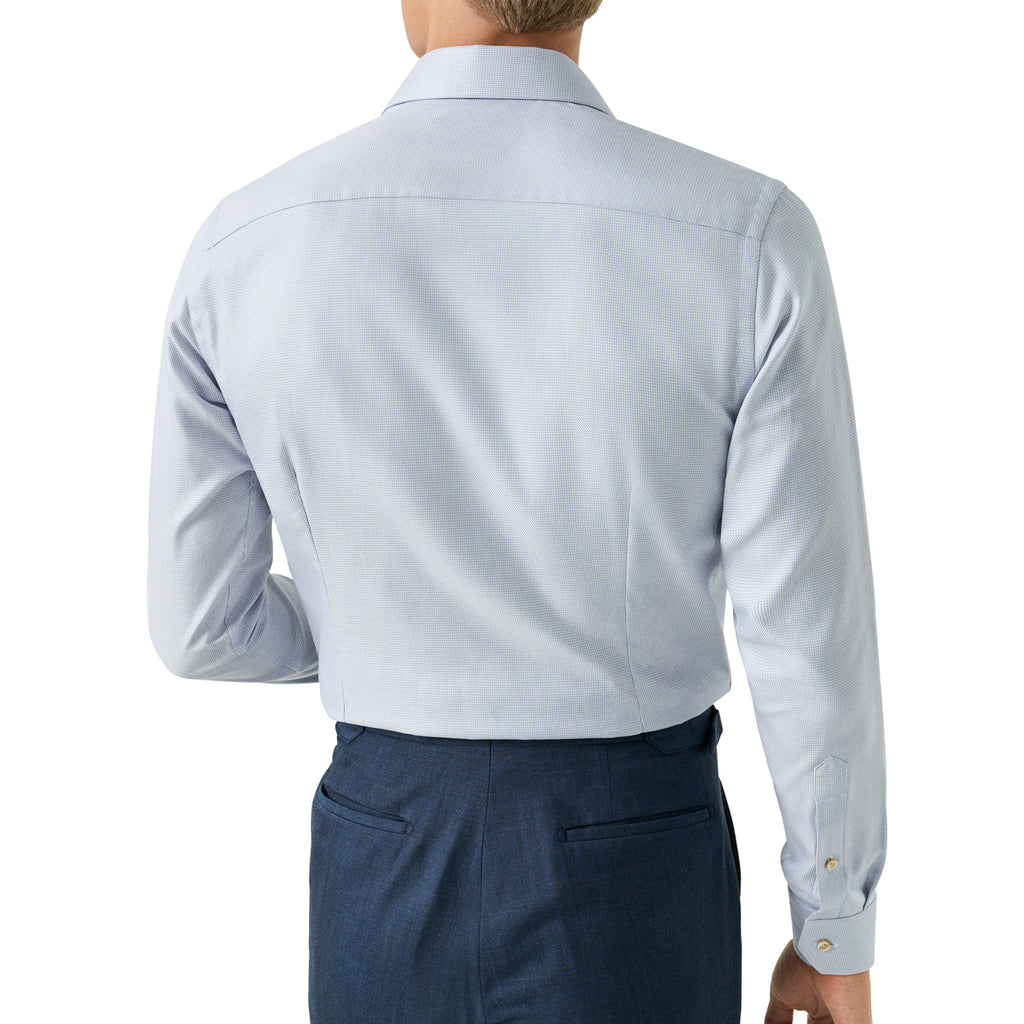Rear view of a man wearing a light blue long-sleeve dress shirt and navy trousers against a plain white background. Eton Shirt available at Sakks Menswear in Southampton.