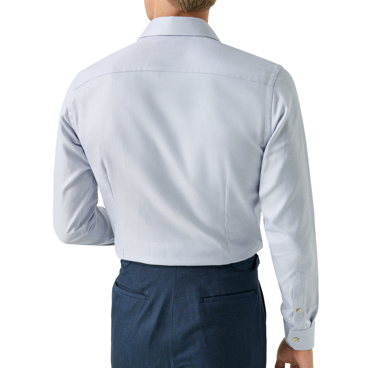Rear view of a man wearing a light blue long-sleeve dress shirt and navy trousers against a plain white background. Eton Shirt available at Sakks Menswear in Southampton.