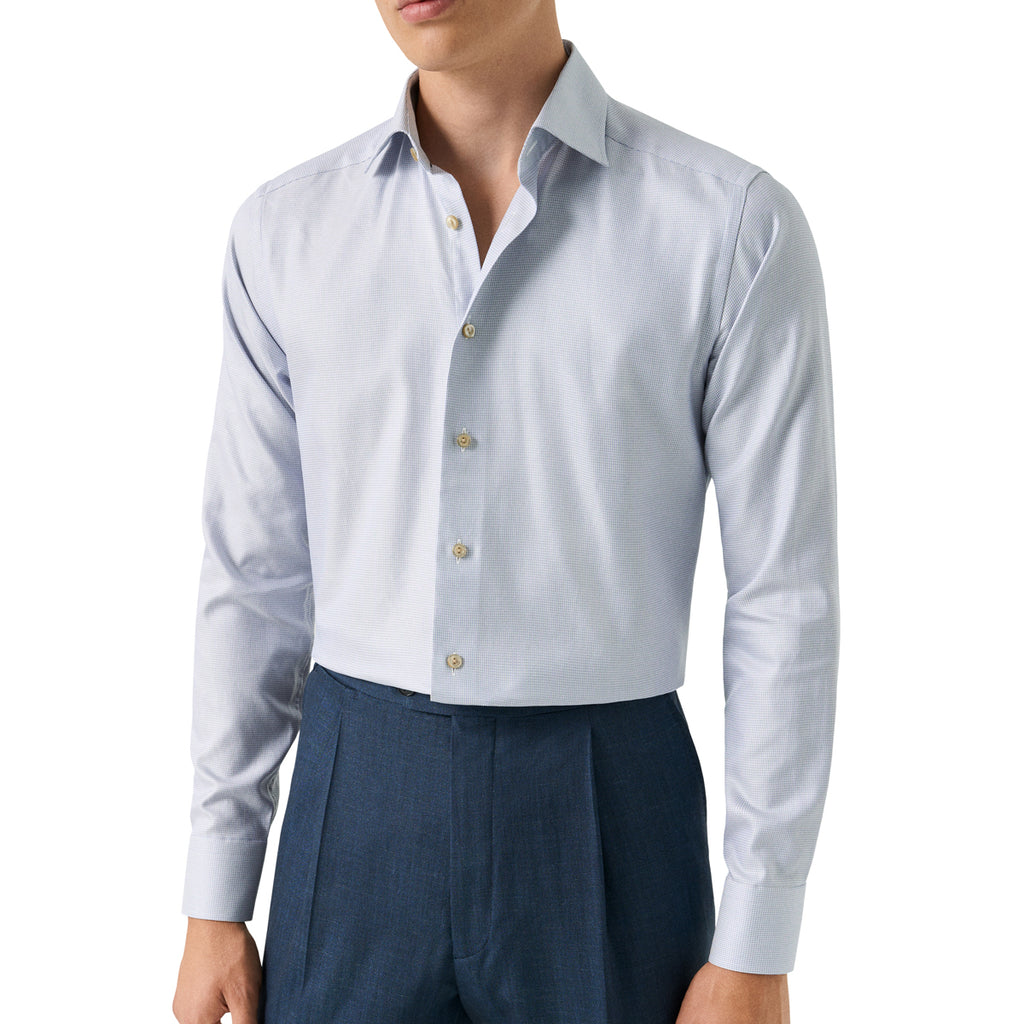 A man wearing a light blue long-sleeve dress shirt tucked into dark blue pleated trousers, shown from the chin down against a plain white background. Eton Shirt available at Sakks Menswear in Southampton.