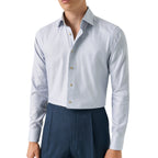 A man wearing a light blue long-sleeve dress shirt tucked into dark blue pleated trousers, shown from the chin down against a plain white background. Eton Shirt available at Sakks Menswear in Southampton.