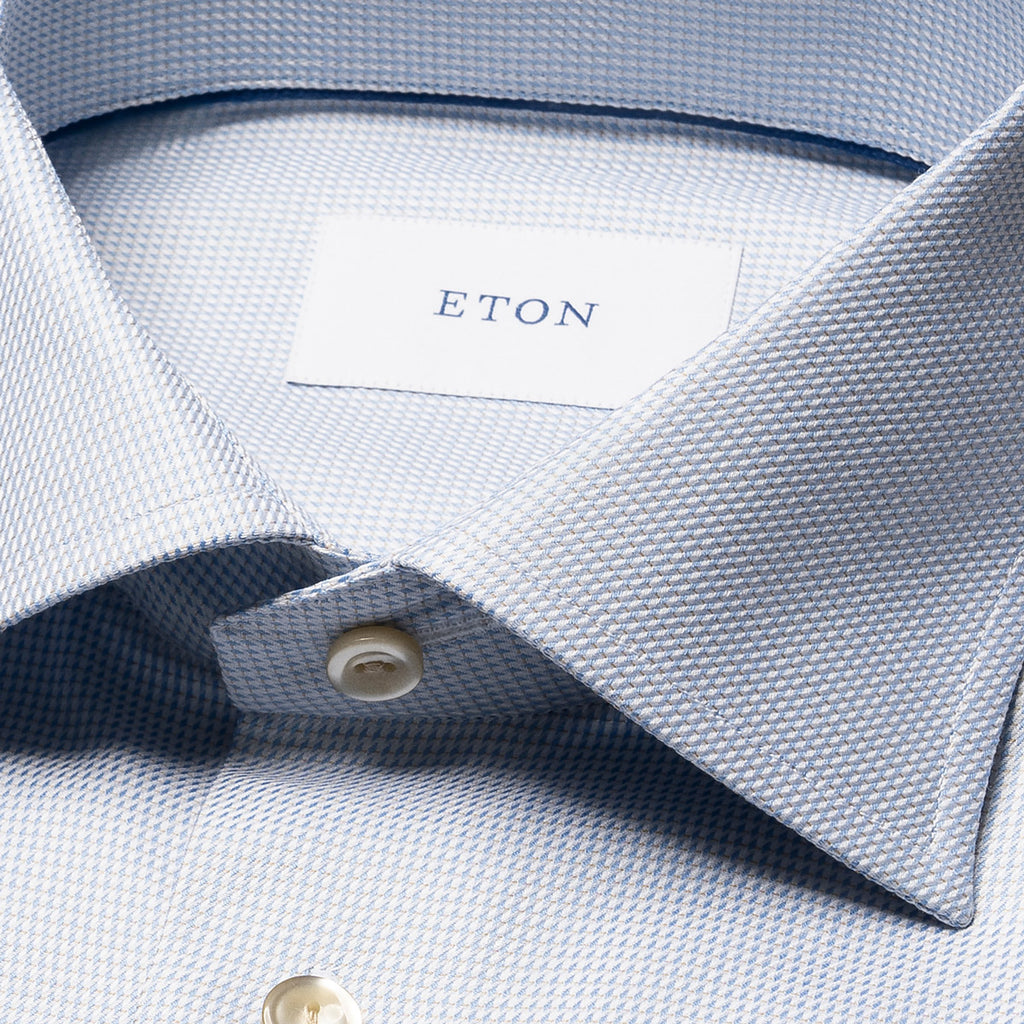 Close-up of a light blue and white micro-patterned dress shirt collar with a white neck label reading ETON. Eton Shirt available at Sakks Menswear in Southampton.