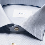 Close-up of a light blue and white micro-patterned dress shirt collar with a white neck label reading ETON. Eton Shirt available at Sakks Menswear in Southampton.