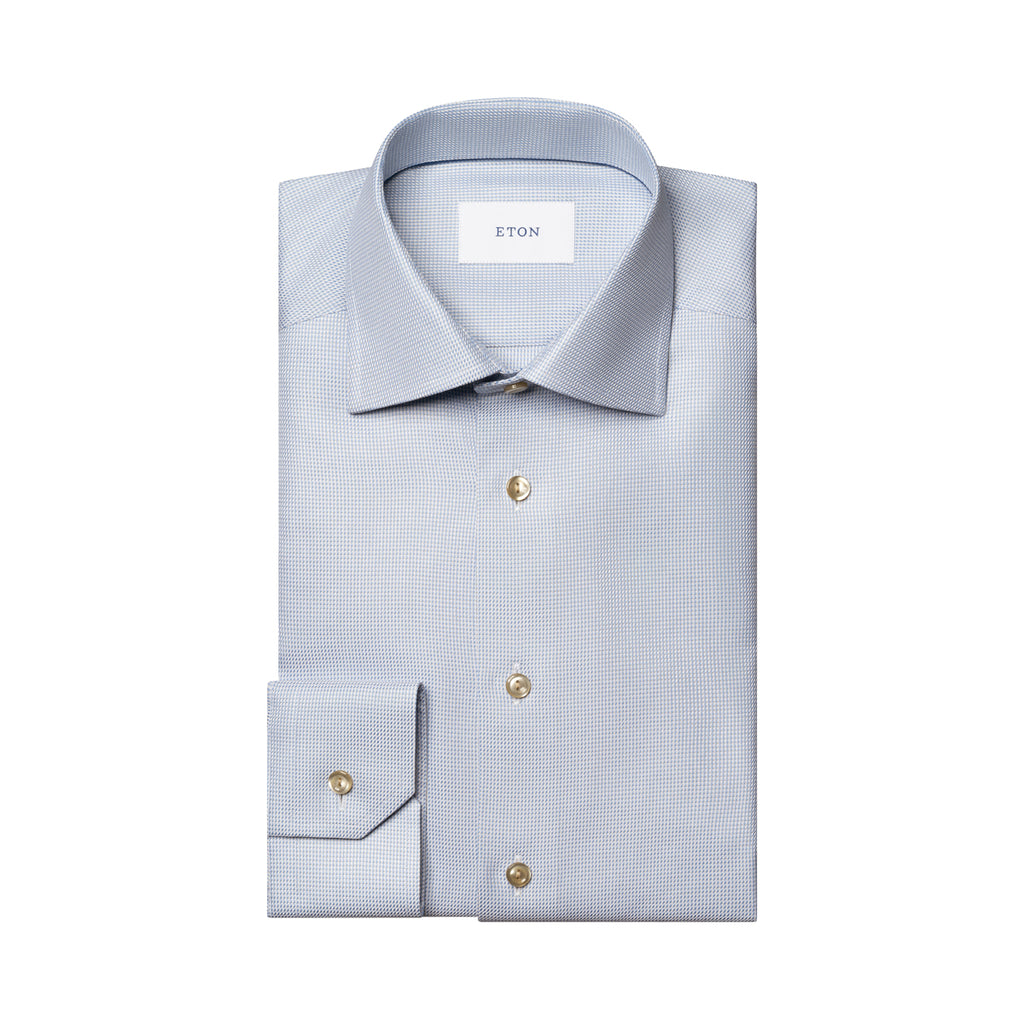A folded light blue dress shirt with a subtle micro-check pattern, featuring gold buttons and a white neck label with the brand name ETON. Eton Shirt available at Sakks Menswear in Southampton.