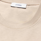 Close-up of a cream-coloured ribbed knit garment, likely a t-shirt, showing the inner neck label with the brand name ETON. Eton T-Shirt available at Sakks Menswear in Southampton.