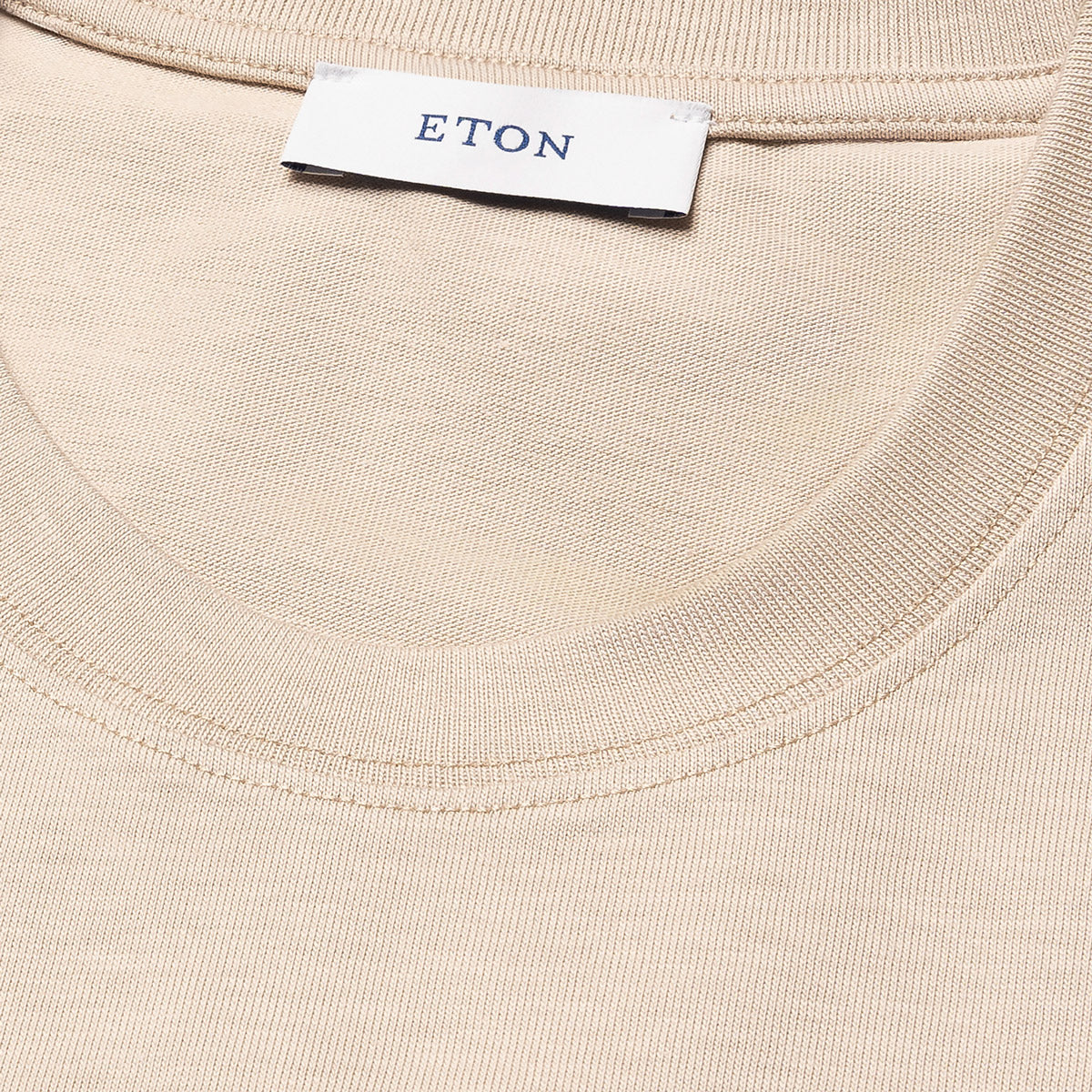 Close-up of a cream-coloured ribbed knit garment, likely a t-shirt, showing the inner neck label with the brand name ETON. Eton T-Shirt available at Sakks Menswear in Southampton.