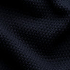 A close-up of dark navy blue textured knit fabric with a waffle or dimple pattern, shown with soft folds and shadows. Eton Polo available at Sakks Menswear in Southampton.