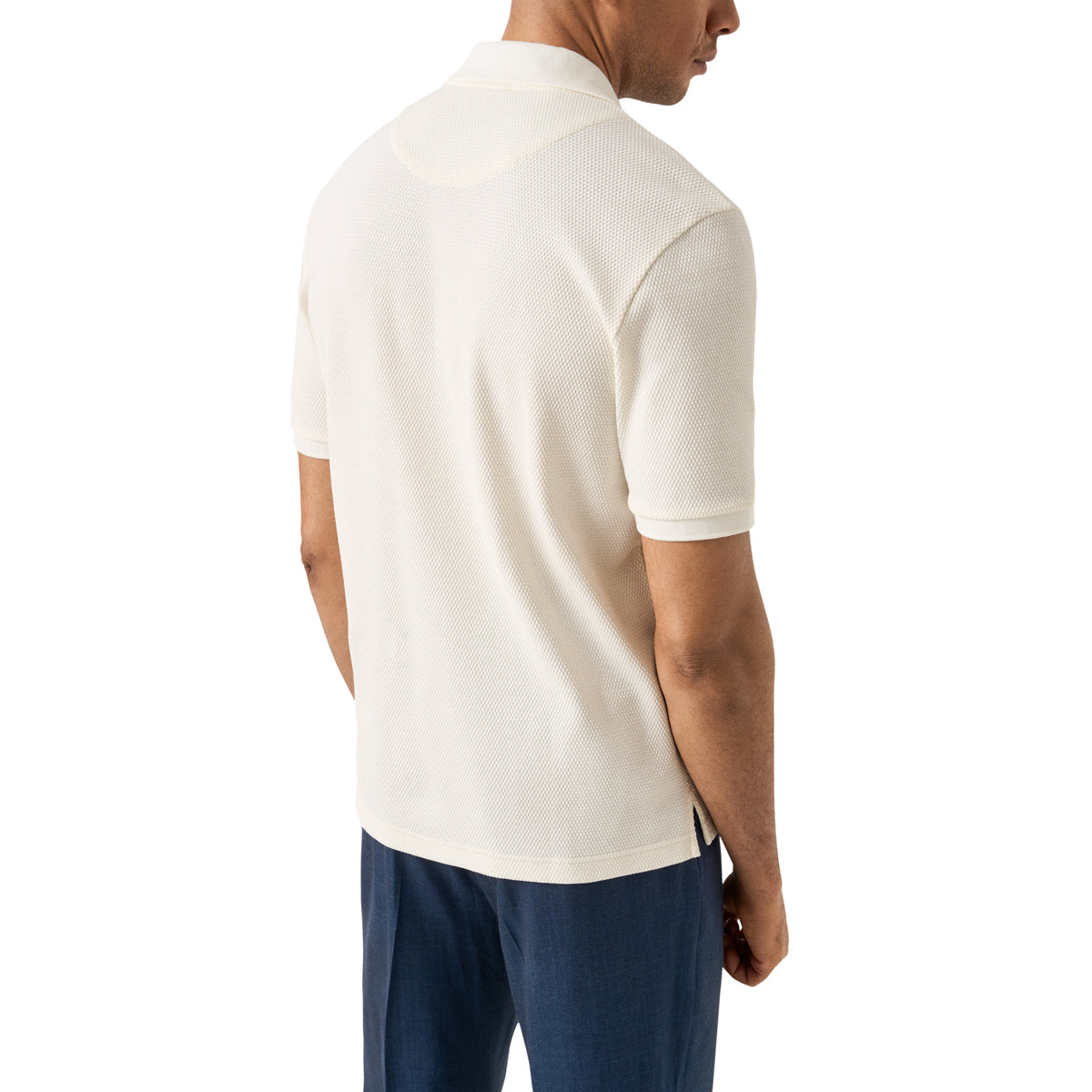 A man wearing a short-sleeve knit polo shirt in off-white, shown from a rear three-quarter view against a plain white background. Eton Polo available at Sakks Menswear in Southampton.