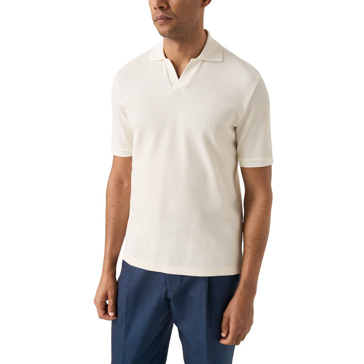 A man wearing a short-sleeve polo shirt in off-white/cream, paired with navy blue trousers, photographed against a plain white studio background. Eton Polo available at Sakks Menswear in Southampton.