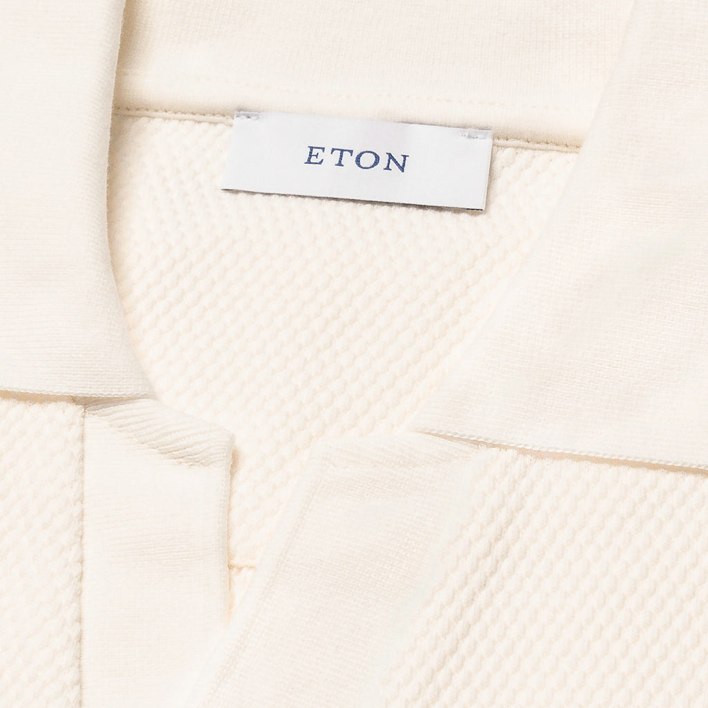 Close-up of a cream-colored textured knit garment, showing a white brand label with the name ETON printed in navy blue. Eton Polo available at Sakks Menswear in Southampton.