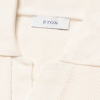 Close-up of a cream-colored textured knit garment, showing a white brand label with the name ETON printed in navy blue. Eton Polo available at Sakks Menswear in Southampton.