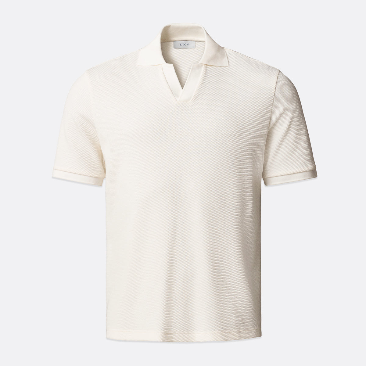 An off-white short-sleeve polo shirt with a textured knit fabric, displayed on a clean, light grey background. Eton Polo available at Sakks Menswear in Southampton.