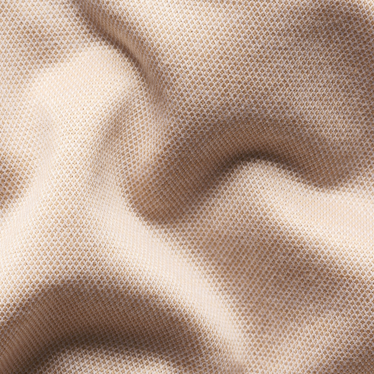 A close-up of draped beige fabric with a fine mesh or woven texture, showing soft folds and shadows. Eton Polo Available at Sakks Menswear in Southampton.