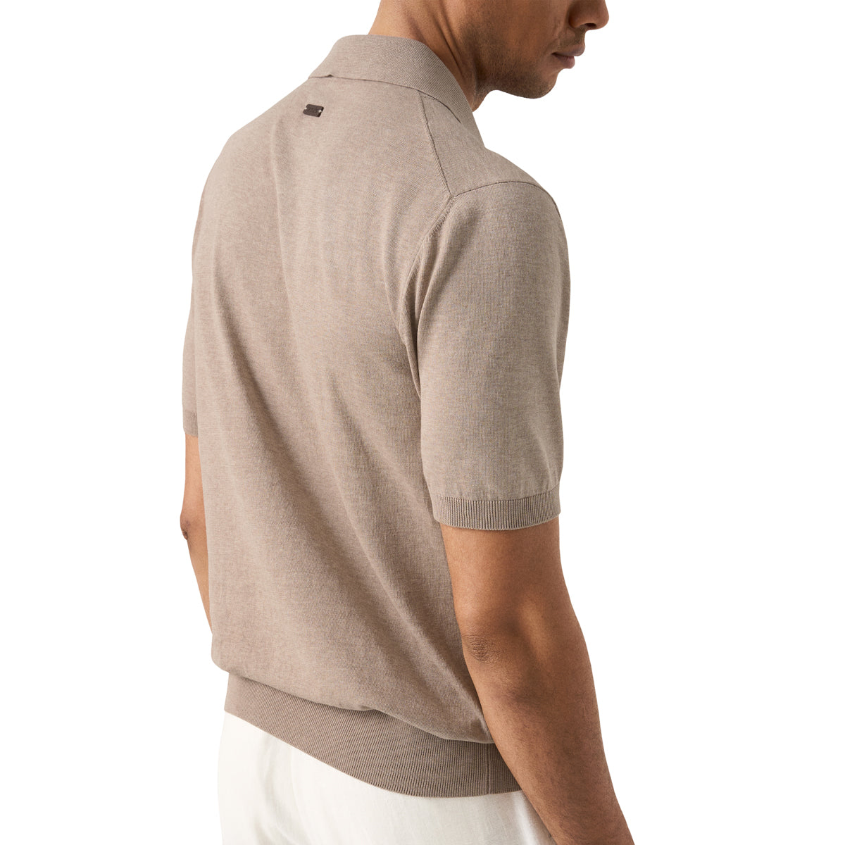 A man wearing a light taupe short-sleeve knit polo shirt, shown from a side-back angle against a plain white background. Eton Knitted Polo available at Sakks Menswear in Southampton.