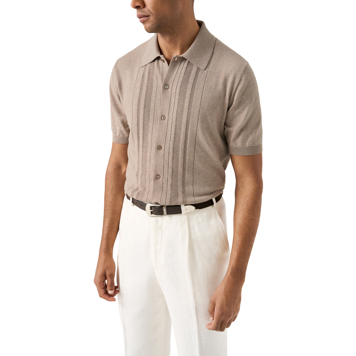 A man wearing a light taupe short-sleeve knit polo shirt with vertical pleats on the front, paired with white trousers and a black belt, shown against a plain white background. Eton Knitted Polo available at Sakks Menswear in Southampton.