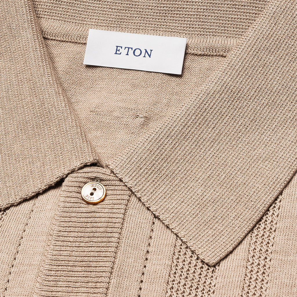Close-up of a beige ribbed knit polo shirt collar with a white neck label reading ETON and a single light-colored button. Eton Knitted Polo available at Sakks Menswear in Southampton.