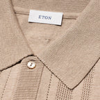 Close-up of a beige ribbed knit polo shirt collar with a white neck label reading ETON and a single light-colored button. Eton Knitted Polo available at Sakks Menswear in Southampton.