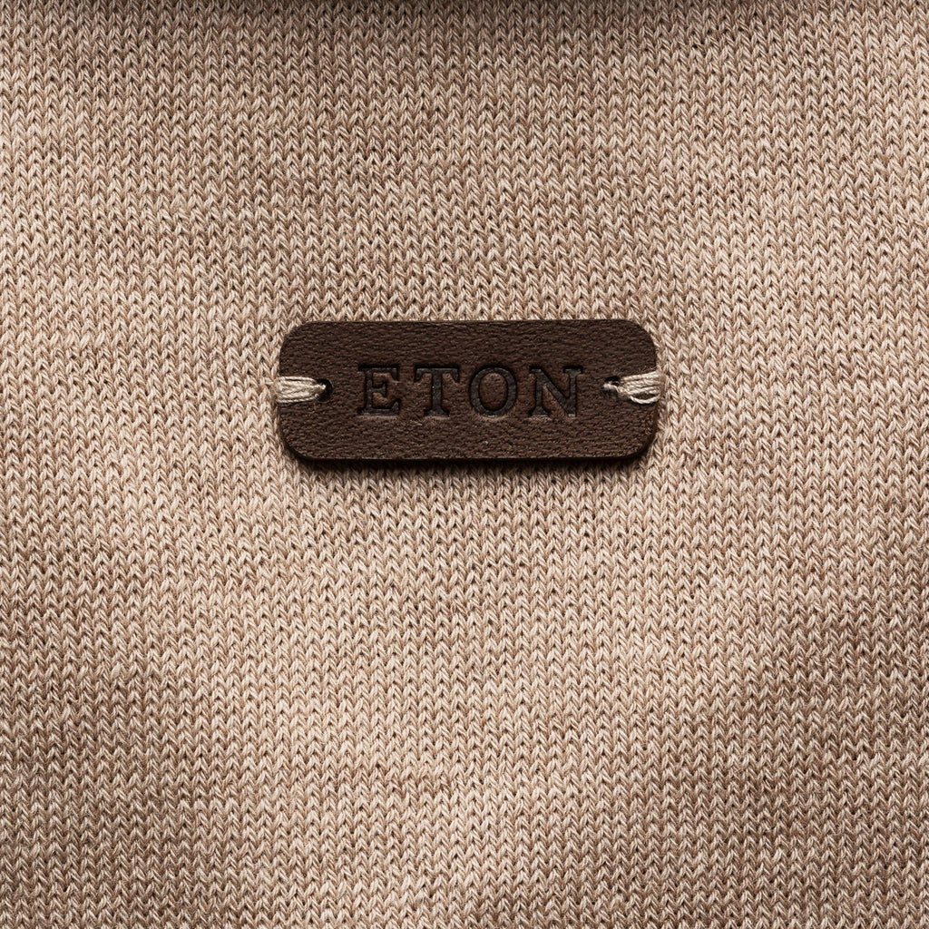 A close-up of a beige knit fabric with a dark brown leather patch in the center embossed with the brand name 'ETON'. Eton Knitted Polo available at Sakks Menswear in Southampton.