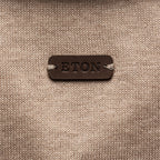 A close-up of a beige knit fabric with a dark brown leather patch in the center embossed with the brand name 'ETON'. Eton Knitted Polo available at Sakks Menswear in Southampton.