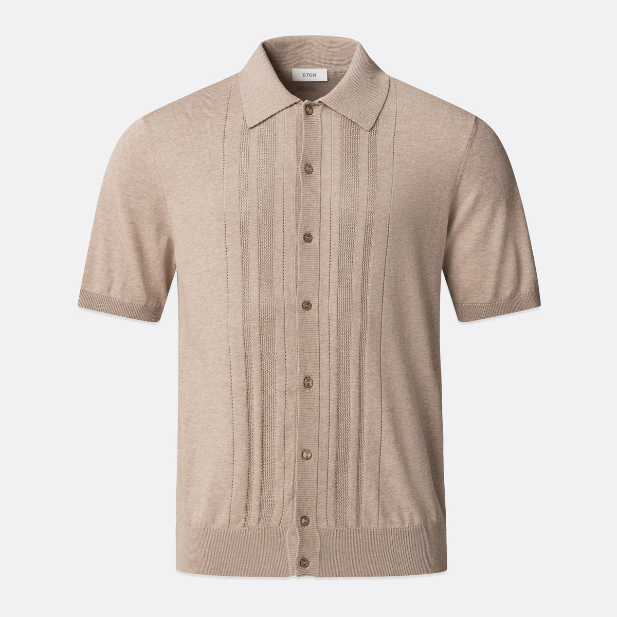 A beige short-sleeve knit polo shirt with vertical pleat details on the front, a button-down front, and a classic collar, shown against a light grey background. Eton Knitted Polo available at Sakks Menswear in Southampton.