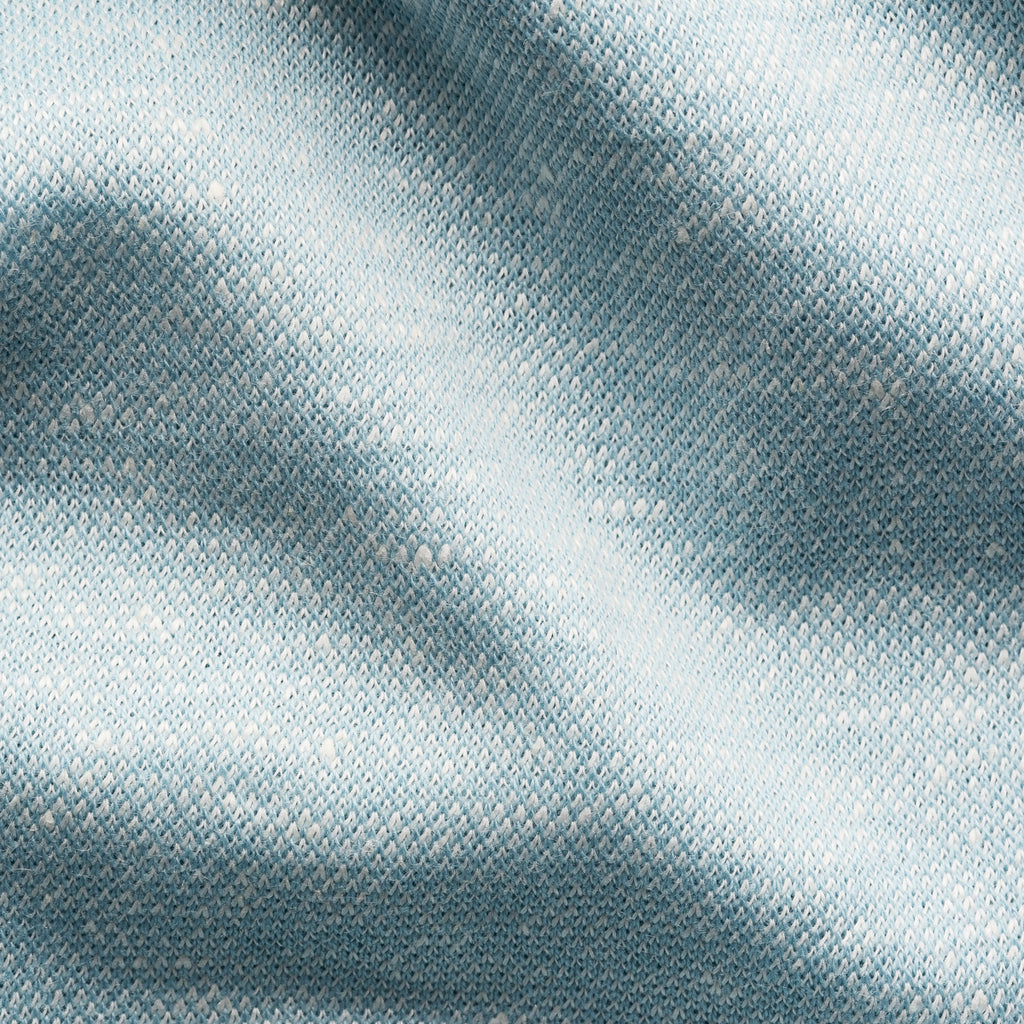 A close-up of textured fabric with a fine woven pattern in a light blue-gray color, showing soft folds and highlights. Eton Polo available at Sakks Menswear in Southampton.