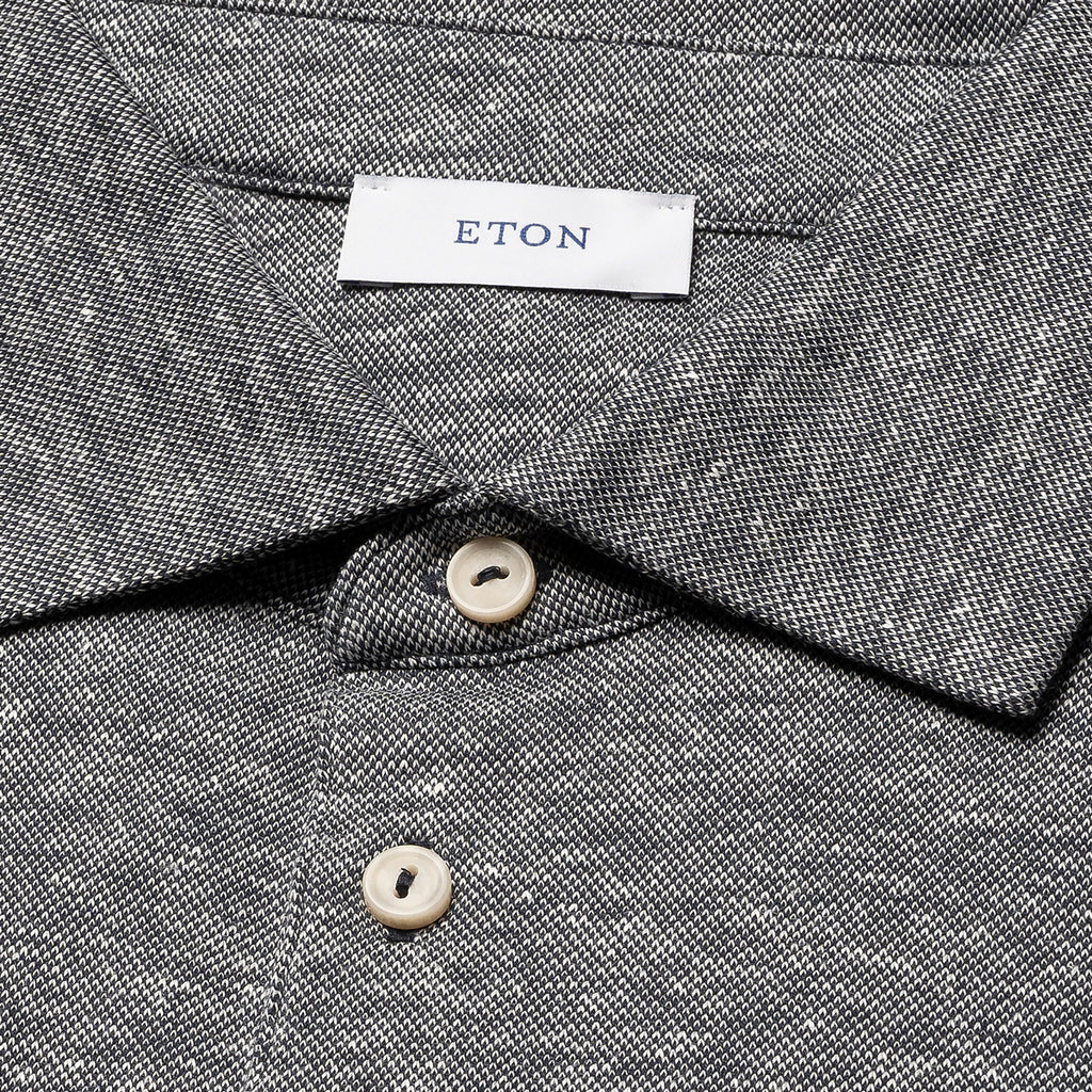 Close-up of a textured grey woven shirt collar with a white neck label reading ETON and two cream buttons. Eton Polo. Sakks Menswear Southampton.