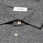 Close-up of a textured grey woven shirt collar with a white neck label reading ETON and two cream buttons. Eton Polo. Sakks Menswear Southampton.