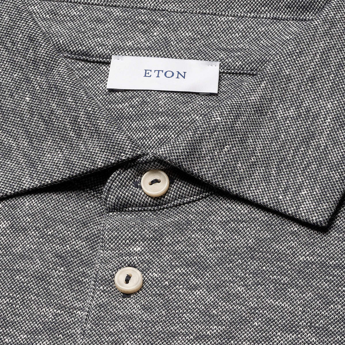 Close-up of a textured grey woven shirt collar with a white neck label reading ETON and two cream buttons. Eton Polo. Sakks Menswear Southampton.