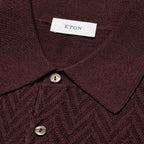 Close-up of a dark burgundy knit polo shirt with a textured herringbone pattern, featuring a white neck label with the brand name 'ETON' and two silver buttons. Eton Polo. Sakks Menswear Southampton.