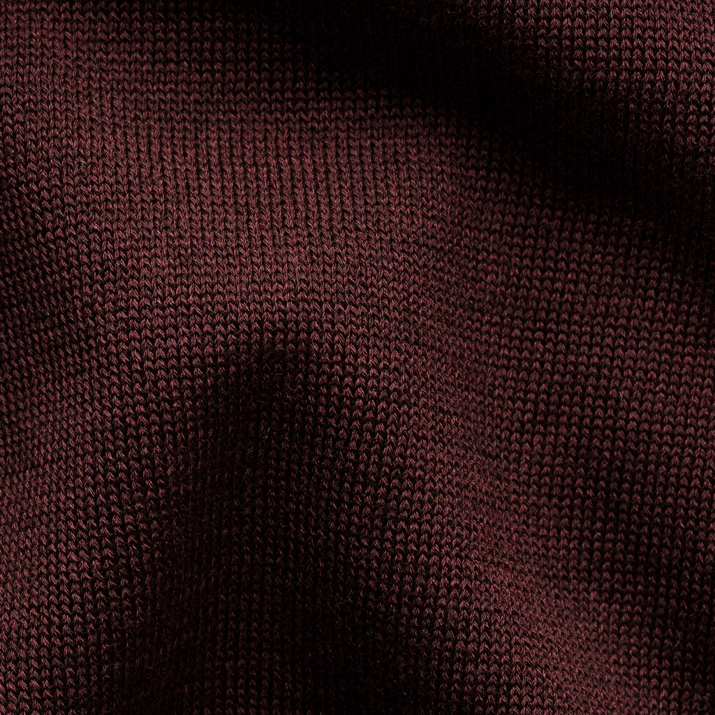 A close-up of a dark burgundy knit fabric texture with soft shadows across the surface. Eton Polo. Sakks Menswear Southampton.