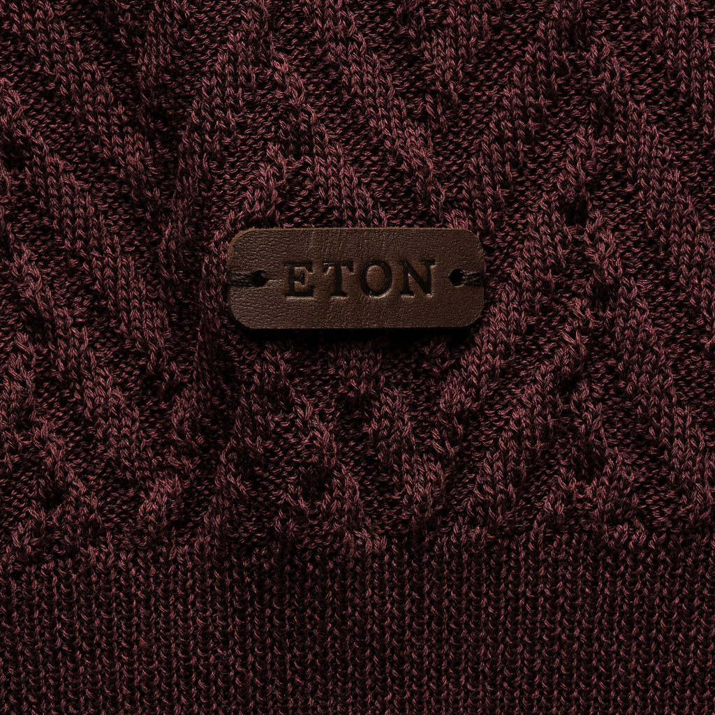 Close-up of a textured knit sweater in deep burgundy with a brown leather patch on the chest embossed with the brand name ETON. Eton Polo. Sakks Menswear Southampton.