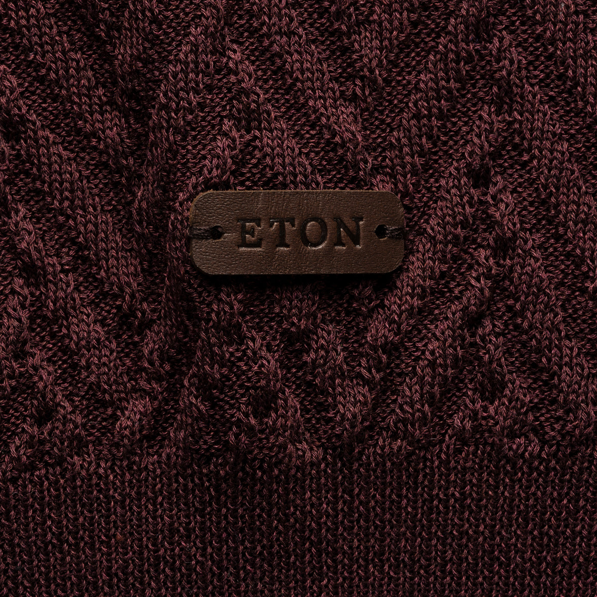 Close-up of a textured knit sweater in deep burgundy with a brown leather patch on the chest embossed with the brand name ETON. Eton Polo. Sakks Menswear Southampton.