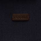 A close-up of a dark brown leather patch embossed with the brand name 'ETON' on a dark navy blue textured fabric background. Eton Shirt Jacket. Sakks Menswear Southampton.