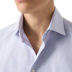 Close-up of a man wearing a light blue and white micro-check patterned dress shirt, showing the collar and chest area. Eton Shirt. Sakks Menswear Southampton.
