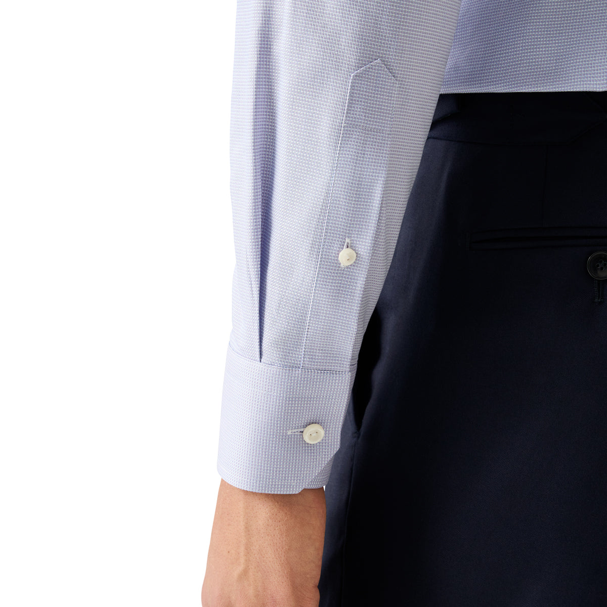 Close-up of a light blue and white micro-check patterned dress shirt cuff with white buttons, worn with dark navy trousers. Eton Shirt. Sakks Menswear Southampton.
