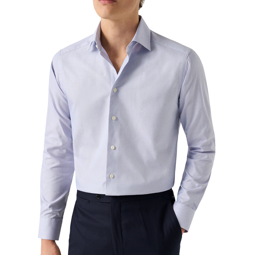 A man wearing a light blue long-sleeve button-down dress shirt with dark navy trousers, shown from the chin down against a plain white background. Eton Shirt. Sakks Menswear Southampton.