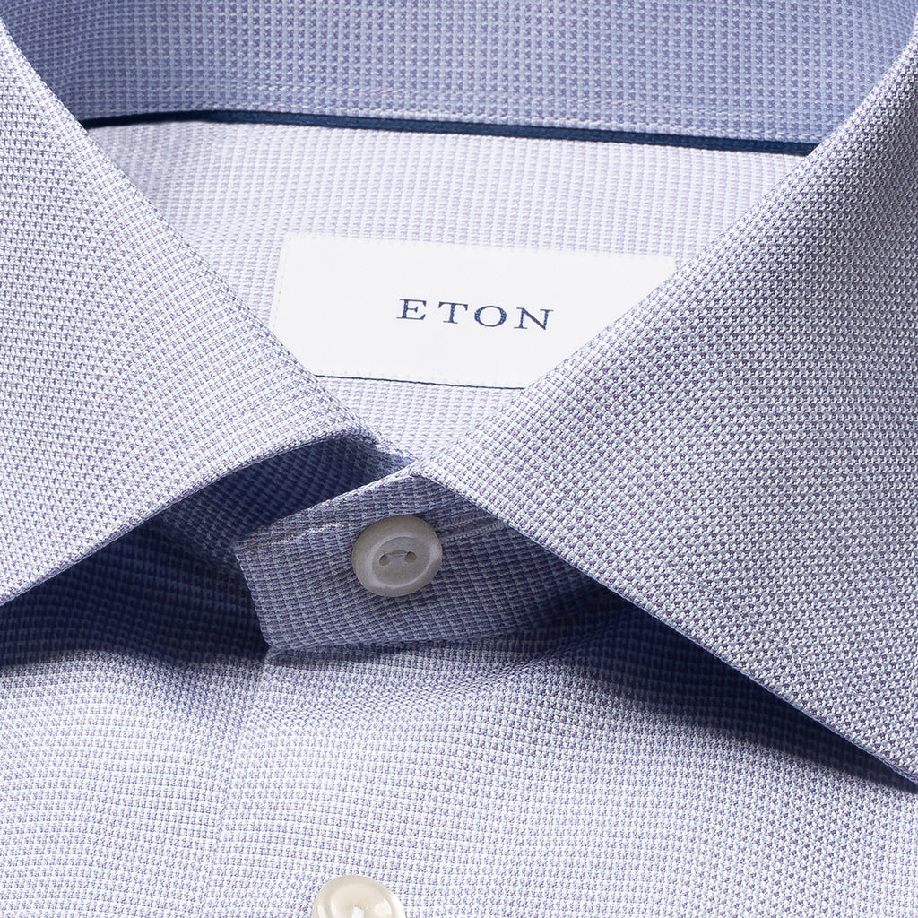 Close-up of a light blue and white micro-check patterned dress shirt collar with a white button and an ETON brand label. Eton Shirt. Sakks Menswear Southampton.