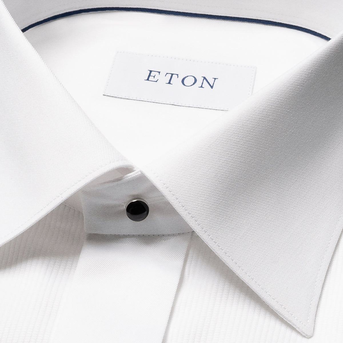 Close-up of a white dress shirt collar with a visible ETON neck label and a single black button. Eton Dinner Shirt. Sakks Menswear Southampton.