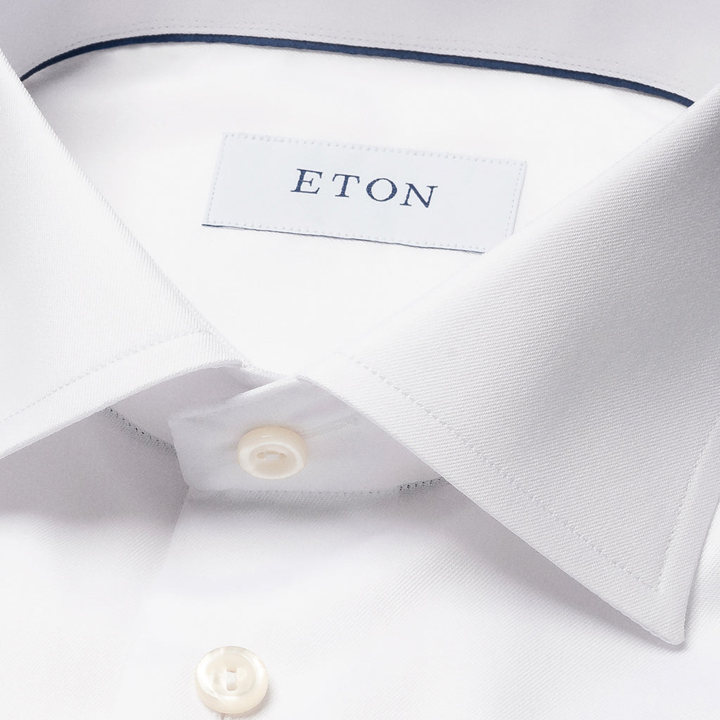 Close-up of a white dress shirt collar with a visible ETON neck label and white buttons, photographed on a clean white background. Eton Shirt. Sakks Menswear Southampton.