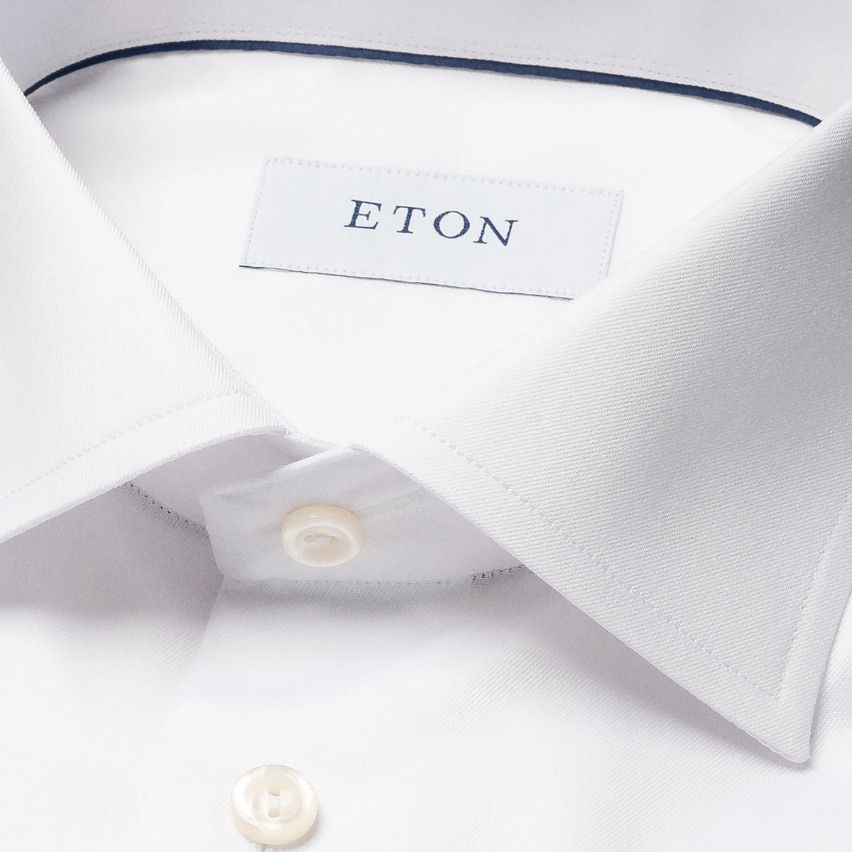 Close-up of a white dress shirt collar with a visible ETON neck label and white buttons, photographed on a clean white background. Eton Shirt. Sakks Menswear Southampton.